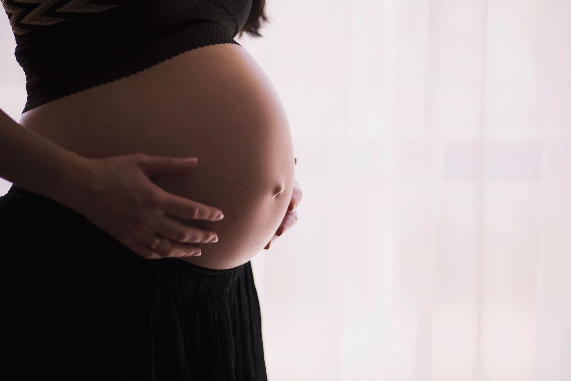 A close-up of a pregnant woman touching her bare belly, expressing warmth and care.